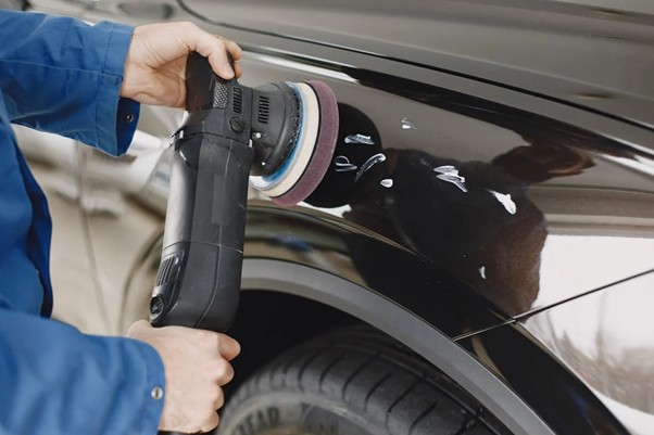 Image showing a person repairing scratches to the side of a black car.